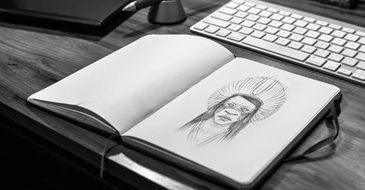 Image monochrome d'un carnet de croquis avec un dessin au crayon sur un bureau en bois avec un ordinateur portable et un clavier.