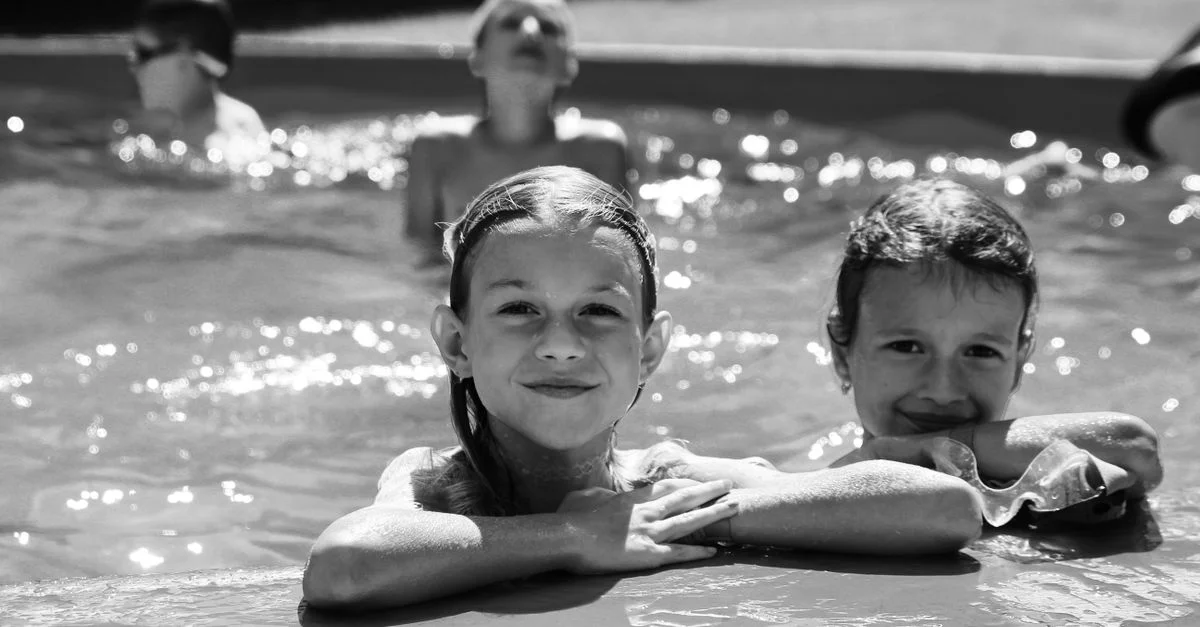 Enfants souriants au bord de la piscine dans une scène d'été ludique en noir et blanc.