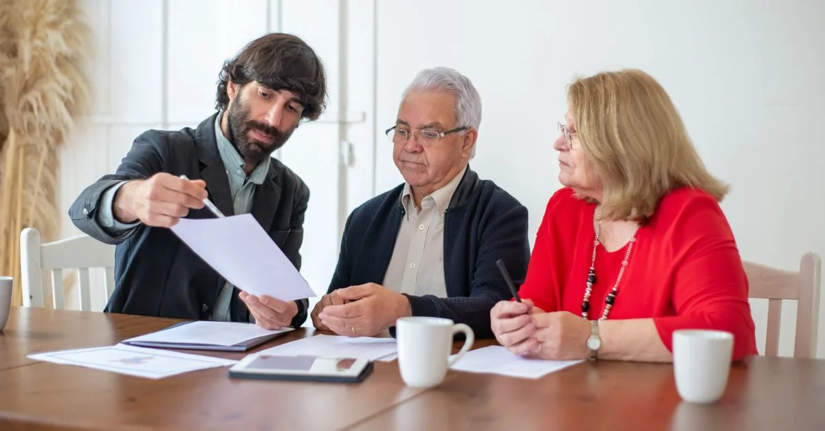 Couple âgé discutant de documents avec un conseiller à une table en bois à l'intérieur.