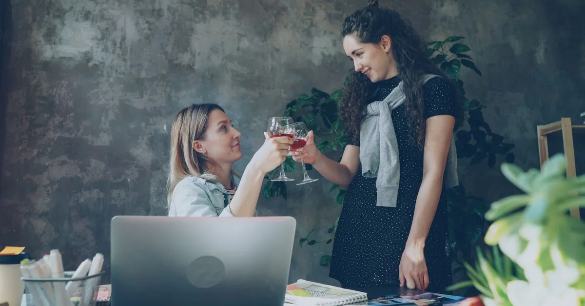 Deux femmes se congratulant avec des verres de vin dans un bureau, célébrant le succès.