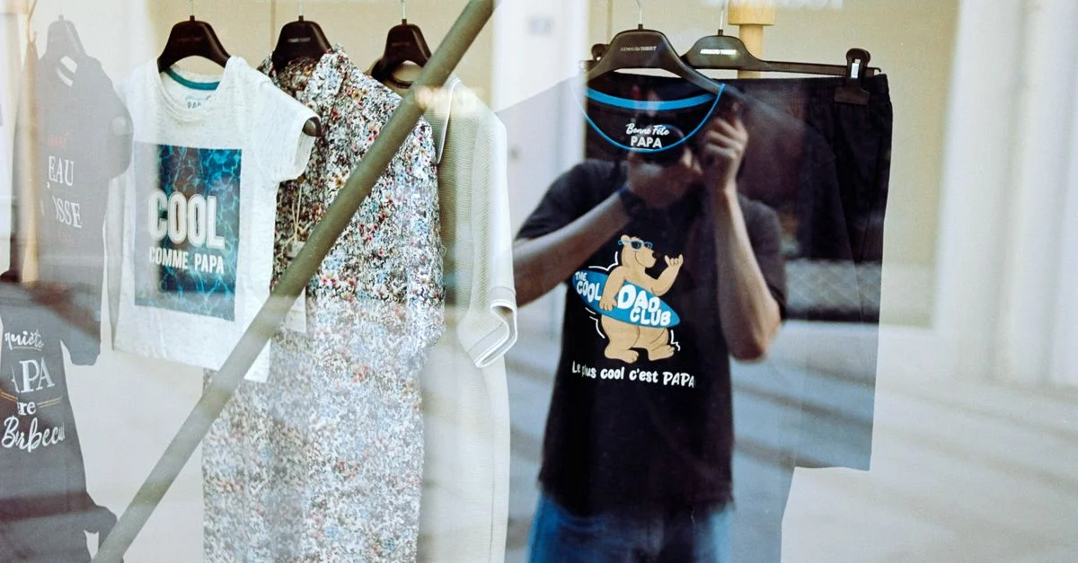 Reflet de vêtements suspendus dans la vitrine d'un magasin de mode affichant des vêtements décontractés et du texte.