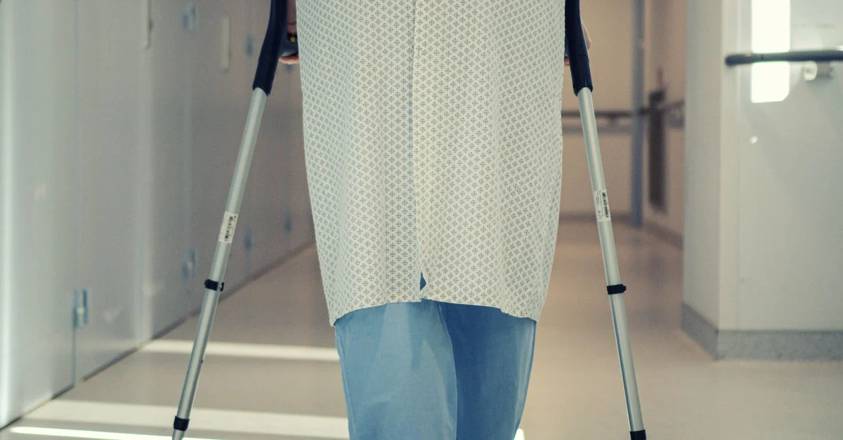 Un patient senior utilisant des béquilles pour marcher dans un couloir d'hôpital, symbolisant la récupération et l'assistance à la mobilité.