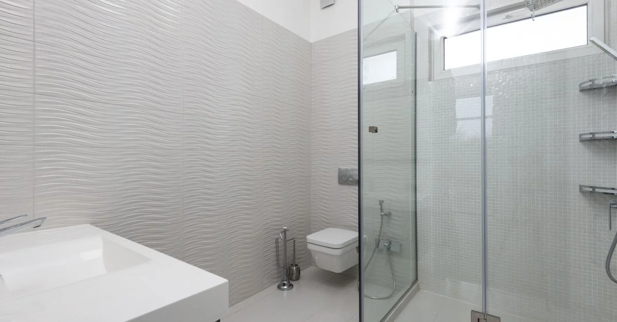 Salle de bains moderne épurée avec douche en verre et murs texturés.