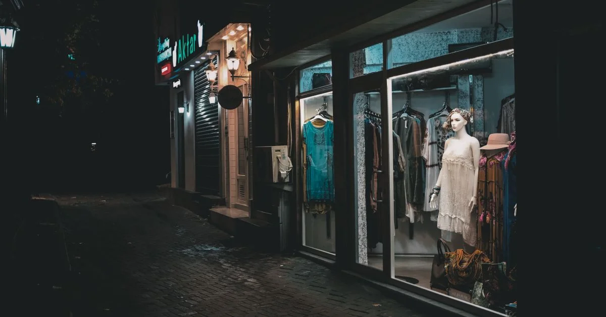 Une vitrine de mode d'une boutique brillamment éclairée dans une ruelle sombre la nuit, mettant en valeur des robes élégantes.