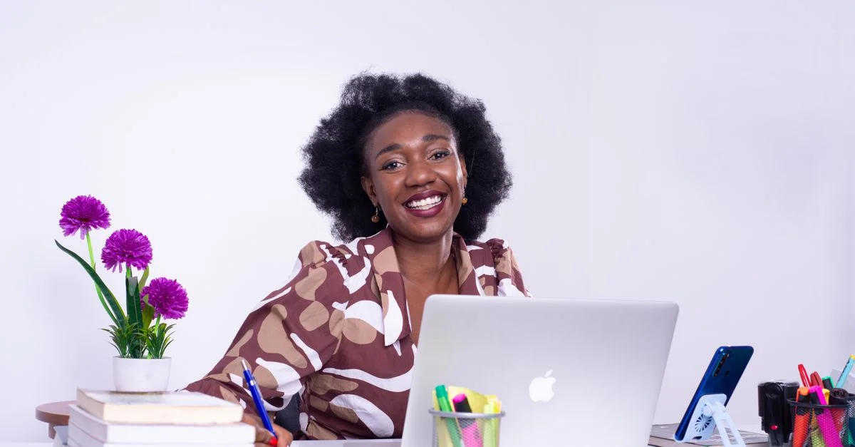 Une femme d'affaires africaine enjouée travaillant à son bureau à Kinshasa, montrant un espace de travail professionnel vivant.