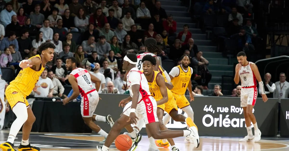 Des joueurs en action lors d'un match de basket-ball en salle, avec une foule qui regarde attentivement.